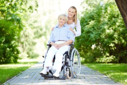 Pretty nurse and senior patient in a wheelchair looking at camera outside